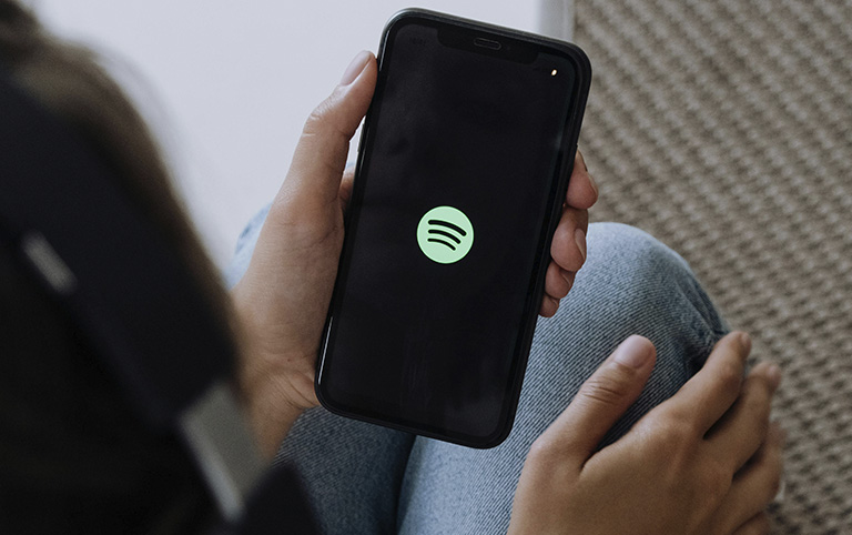 Fotografia colorida de uma pessoa segurando um celular com o logo do Spotify - por Cottonbro - Pexels 