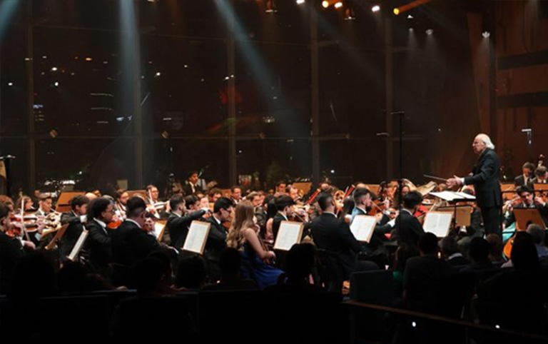 Fotografia colorida de Orquestra Sinfônica Heliópolis e maestro Isaac Karabtchevsky em concerto 